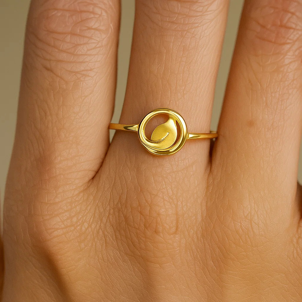 Gold ring with a leaf design on a person's finger against a neutral background