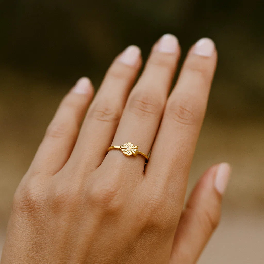 Gold ring with a leaf design on a person's finger against a blurred background